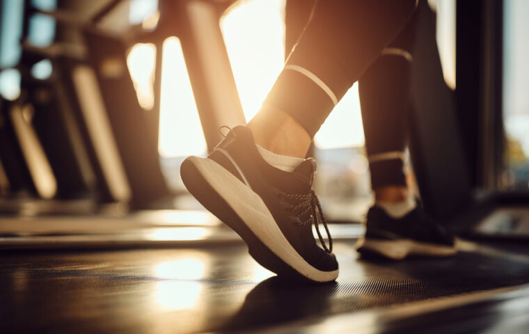Close-up of athletic woman warming up for sports training while walking on treadmill in a gym.