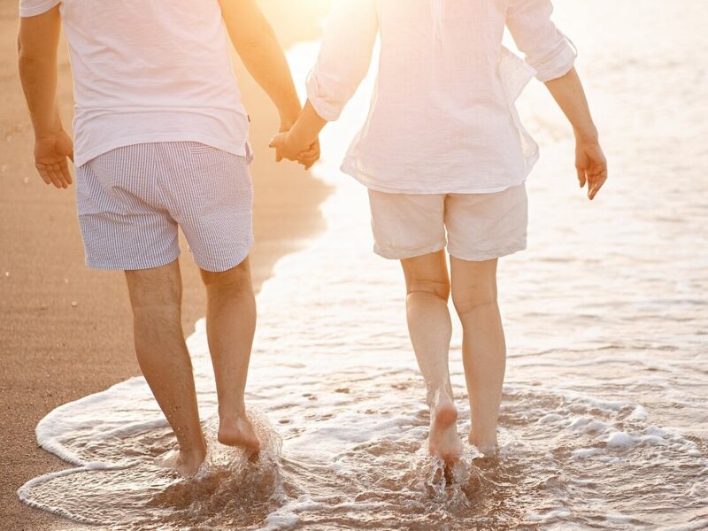 Happy mature senior couple walking and looking at each other on beach during sunset. Aging together and retirement lifestyle concept